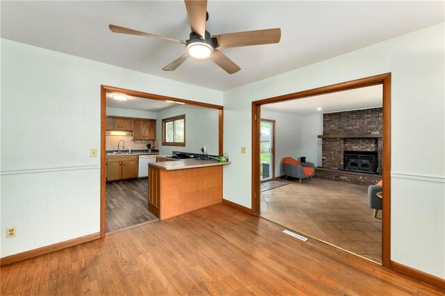 4820 Stearns Ln, Shawnee, KS 66203 - kitchen featuring white dishwasher, open floor plan, brown cabinetry, a peninsula, and a brick fireplace