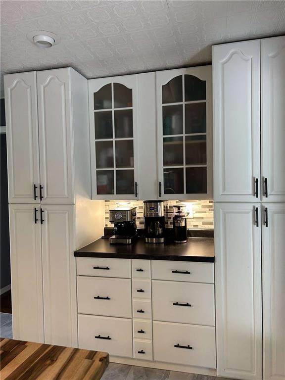 241 E S St, Peculiar, MO 64078 - kitchen featuring dark countertops, glass insert cabinets, white cabinetry, and an ornate ceiling