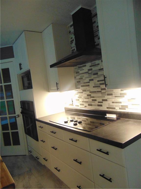 241 E S St, Peculiar, MO 64078 - kitchen featuring wall chimney exhaust hood, black oven, electric cooktop, marble finish floors, and white cabinets