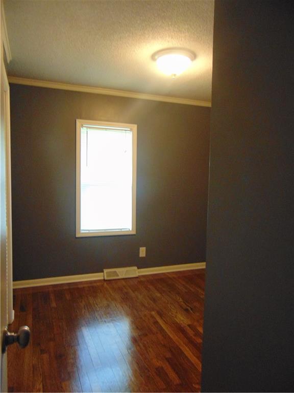 241 E S St, Peculiar, MO 64078 - empty room featuring wood finished floors, crown molding, and a textured ceiling