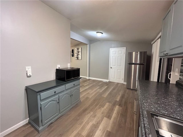 409 N Geronimo Dr, Independence, MO 64056 - kitchen with freestanding refrigerator, black microwave, dark countertops, wood finished floors, and lofted ceiling
