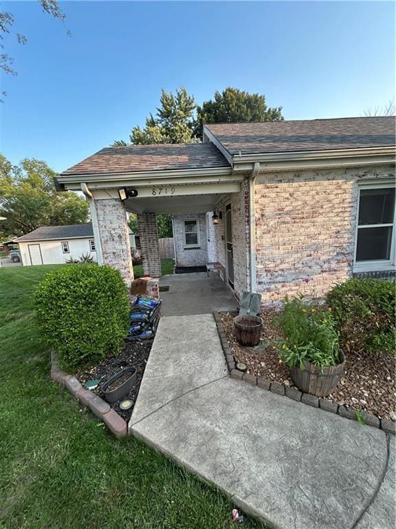 8719 E 57th St, Raytown, MO 64129 - view of exterior entry featuring brick siding, a yard, and roof with shingles