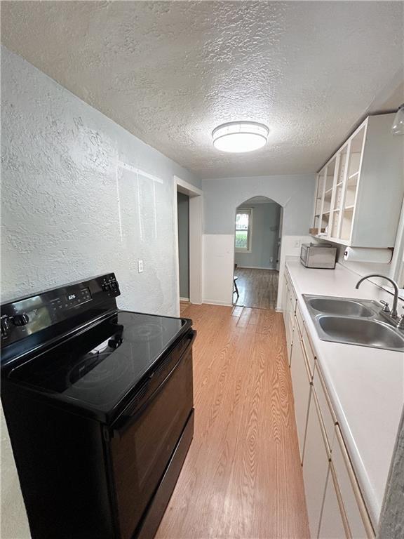 8719 E 57th St, Raytown, MO 64129 - kitchen with black range with electric stovetop, arched walkways, light wood finished floors, a textured ceiling, and a textured wall