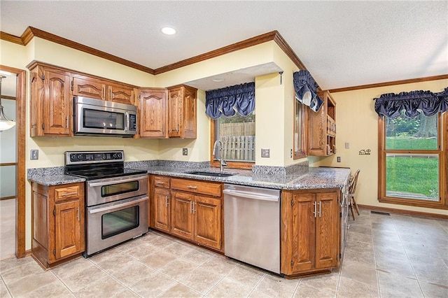 2409 NE 73rd Ter, Gladstone, MO 64118 - kitchen with stainless steel appliances, a sink, brown cabinetry, a textured ceiling, and dark stone counters