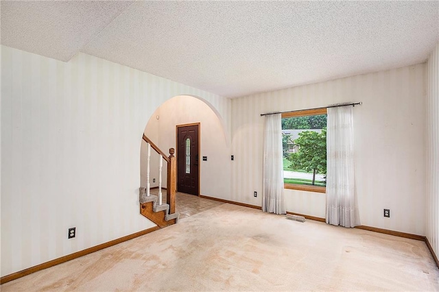 2409 NE 73rd Ter, Gladstone, MO 64118 - unfurnished room with arched walkways, a textured ceiling, baseboards, carpet, and stairway