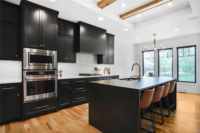 1245 NE Goshen Dr, Lees Summit, MO 64064 - kitchen with appliances with stainless steel finishes, dark cabinets, light wood-style flooring, backsplash, and wall chimney exhaust hood