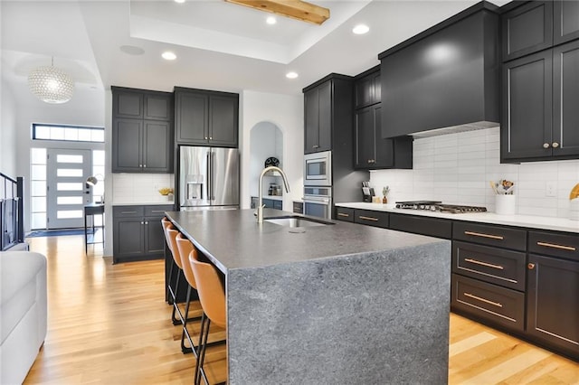 1245 NE Goshen Dr, Lees Summit, MO 64064 - kitchen with appliances with stainless steel finishes, a tray ceiling, light wood finished floors, arched walkways, and recessed lighting