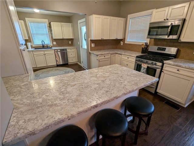 1208 Central Ave, Horton, KS 66439 - kitchen featuring appliances with stainless steel finishes, a kitchen bar, decorative backsplash, white cabinetry, and dark wood-style flooring