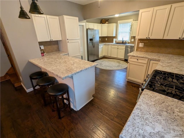 1208 Central Ave, Horton, KS 66439 - kitchen with appliances with stainless steel finishes, dark wood finished floors, decorative backsplash, a kitchen bar, and a peninsula