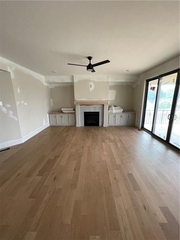 1824 Arbor Trl, Liberty, MO 64068 - unfurnished living room featuring light wood-style floors, a ceiling fan, a textured ceiling, and a fireplace
