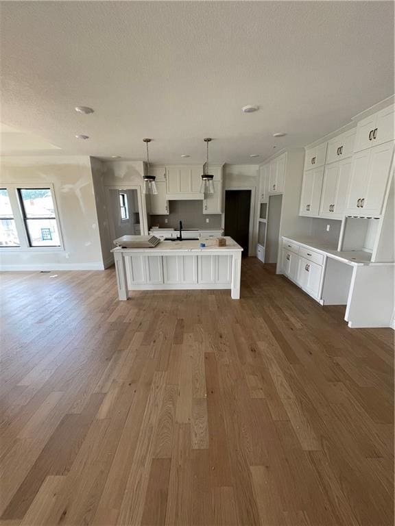 1824 Arbor Trl, Liberty, MO 64068 - kitchen featuring wood finished floors, open floor plan, white cabinets, an island with sink, and a textured ceiling