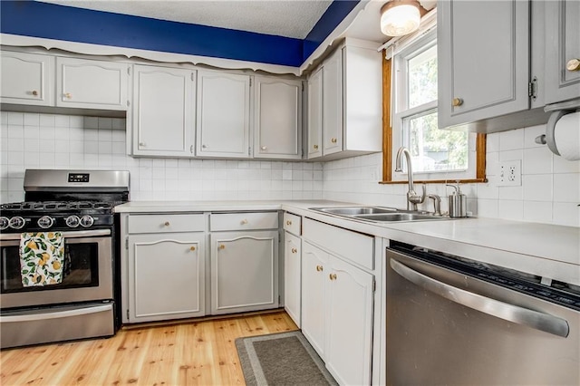 3920 S Milton Dr, Independence, MO 64055 - kitchen with appliances with stainless steel finishes, a sink, light countertops, light wood-style flooring, and backsplash