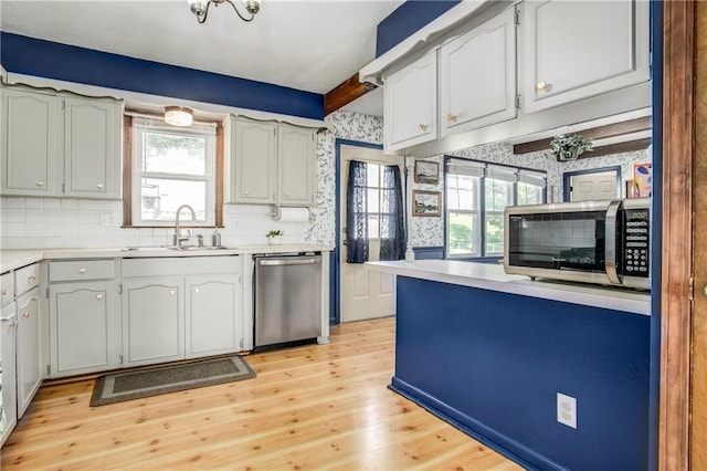 3920 S Milton Dr, Independence, MO 64055 - kitchen with appliances with stainless steel finishes, a sink, light wood-style flooring, light countertops, and tasteful backsplash
