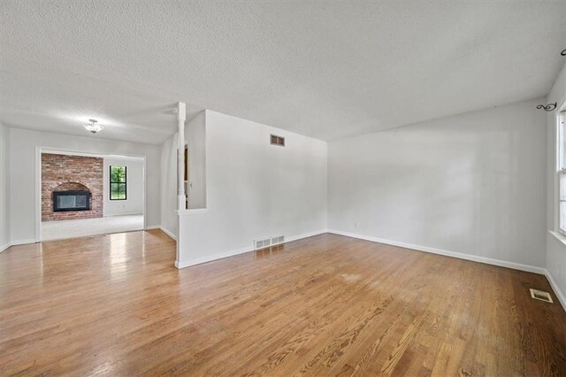 1822 Rankin Dr, Independence, MO 64055 - unfurnished living room featuring wood finished floors, a textured ceiling, and a brick fireplace