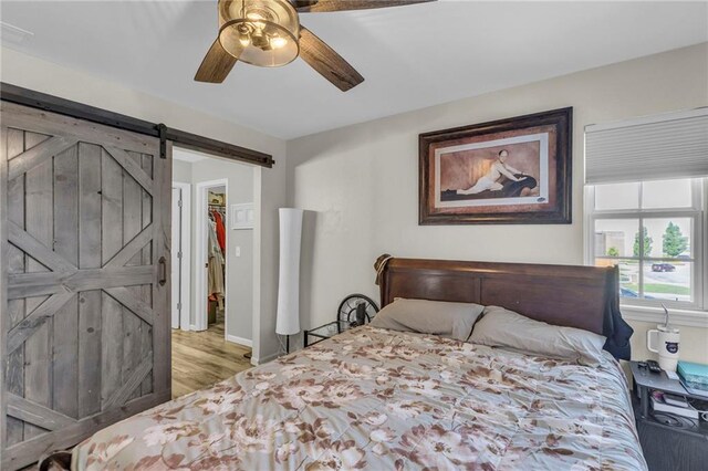 408 Eisenhower Rd, Baldwin City, KS 66006 - bedroom with a barn door, wood finished floors, a spacious closet, and a ceiling fan