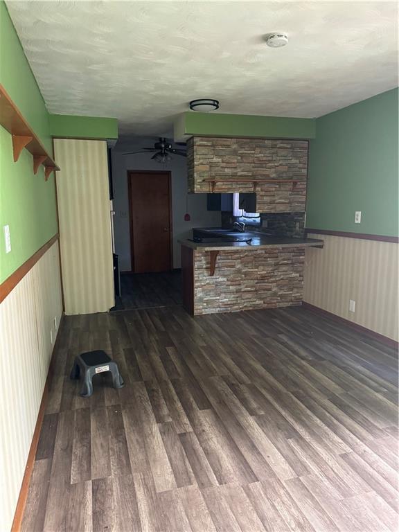 1110 S Plummer Ave, Chanute, KS 66720 - unfurnished living room featuring dark wood finished floors, wainscoting, a ceiling fan, and a fireplace