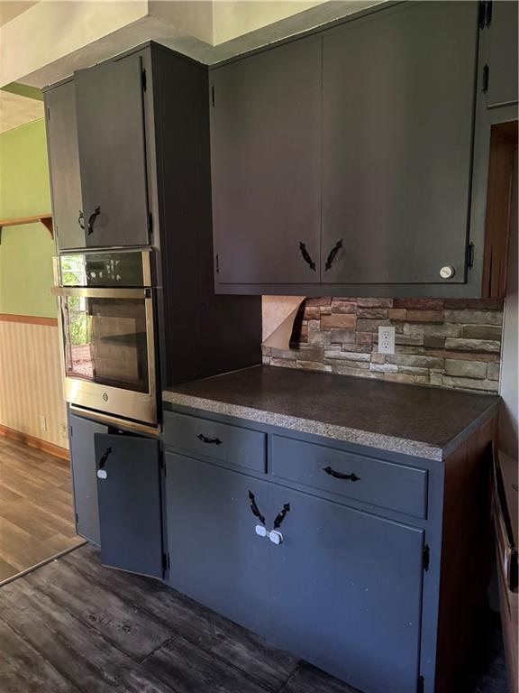 1110 S Plummer Ave, Chanute, KS 66720 - kitchen featuring oven, dark wood-style floors, dark countertops, and backsplash