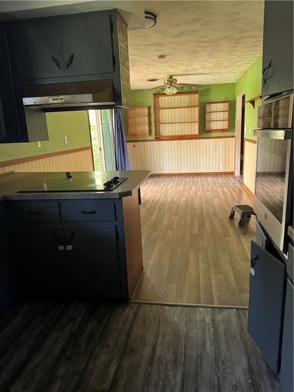 1110 S Plummer Ave, Chanute, KS 66720 - kitchen with black electric stovetop, ventilation hood, dark wood-type flooring, oven, and a peninsula