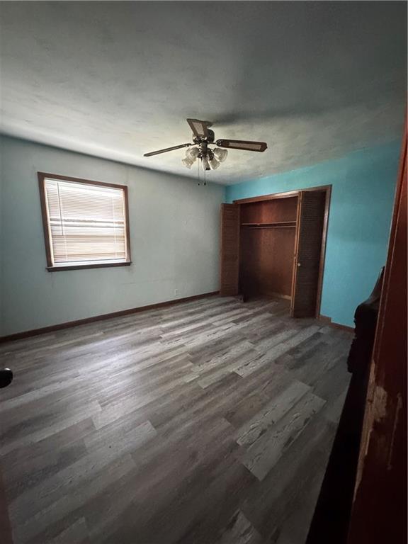 1110 S Plummer Ave, Chanute, KS 66720 - unfurnished bedroom with wood finished floors, baseboards, a ceiling fan, and a closet