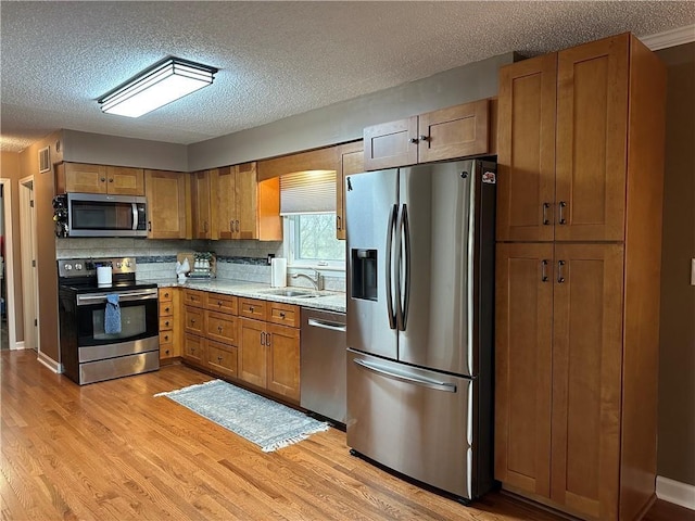 26609 S Red Bud Rd, Freeman, MO 64746 - kitchen featuring stainless steel appliances, light wood-style floors, a textured ceiling, brown cabinetry, and backsplash