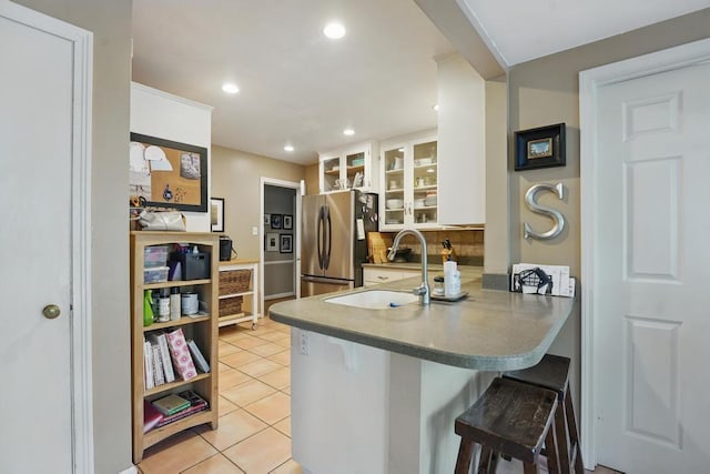 8604 Sagamore Rd, Leawood, KS 66206 - kitchen with freestanding refrigerator, a peninsula, light tile patterned floors, a kitchen breakfast bar, and white cabinetry