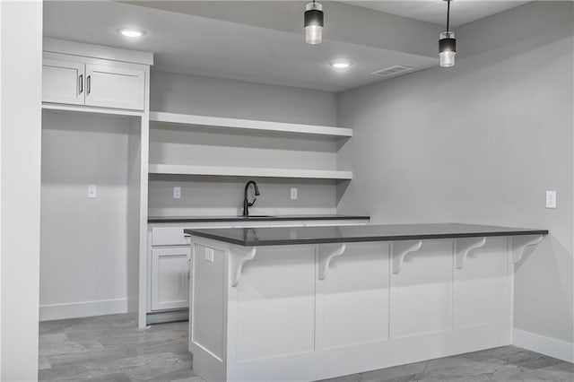 6113 Barth Rd, Shawnee, KS 66226 - kitchen featuring dark countertops, baseboards, hanging light fixtures, a breakfast bar area, and white cabinets