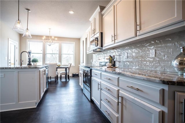 31432 W 85th Ter, De Soto, KS 66018 - kitchen featuring appliances with stainless steel finishes, dark wood-style floors, light stone countertops, tasteful backsplash, and a chandelier