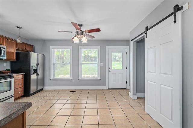 5016 Lydia Ave, Kansas City, MO 64110 - kitchen featuring a barn door, stainless steel appliances, a ceiling fan, dark countertops, and light tile patterned flooring