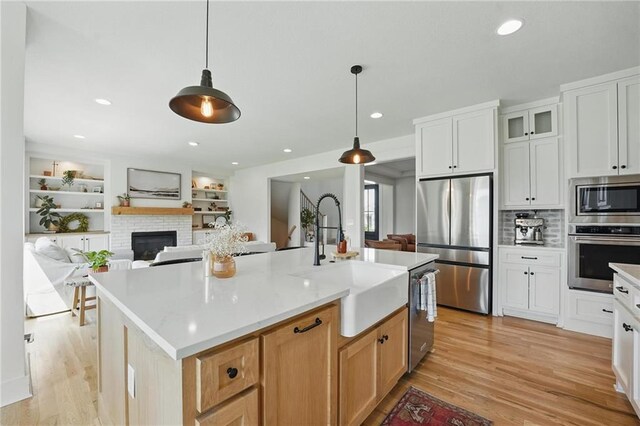 16555 S Lichtenauer Dr, Olathe, KS 66062 - kitchen featuring appliances with stainless steel finishes, light wood finished floors, a brick fireplace, a center island with sink, and decorative light fixtures