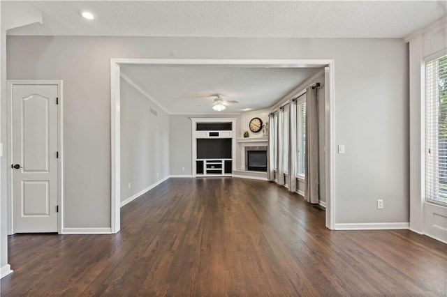 17940 W 158th Ct, Olathe, KS 66062 - unfurnished living room with a ceiling fan, dark wood-type flooring, built in shelves, a glass covered fireplace, and a textured ceiling