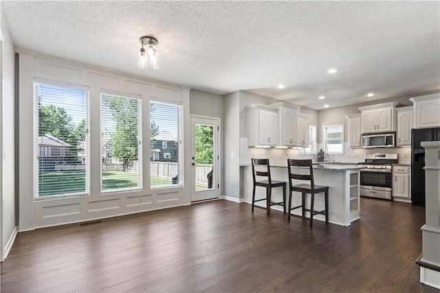 17940 W 158th Ct, Olathe, KS 66062 - kitchen with appliances with stainless steel finishes, a textured ceiling, a kitchen breakfast bar, dark wood-style floors, and white cabinets