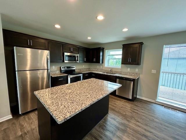 21800 Southcreek Rd, Peculiar, MO 64078 - kitchen with appliances with stainless steel finishes, dark brown cabinetry, dark wood-style flooring, light stone countertops, and a kitchen island
