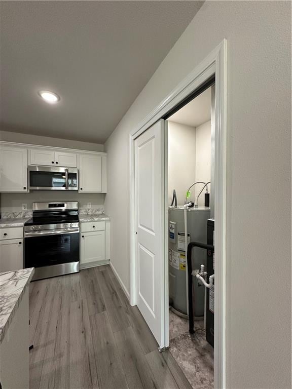 822 Carolina St, Neodesha, KS 66757 - kitchen featuring appliances with stainless steel finishes, water heater, wood finished floors, white cabinetry, and recessed lighting