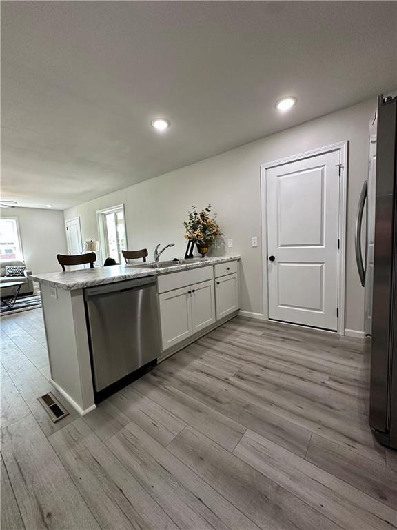 822 Carolina St, Neodesha, KS 66757 - kitchen featuring stainless steel appliances, a peninsula, light wood-style floors, recessed lighting, and light stone countertops