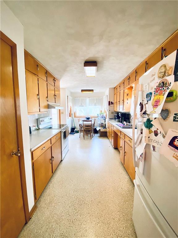 311 SW 12th Ter, Concordia, MO 64020 - kitchen featuring white appliances, light countertops, brown cabinetry, and under cabinet range hood