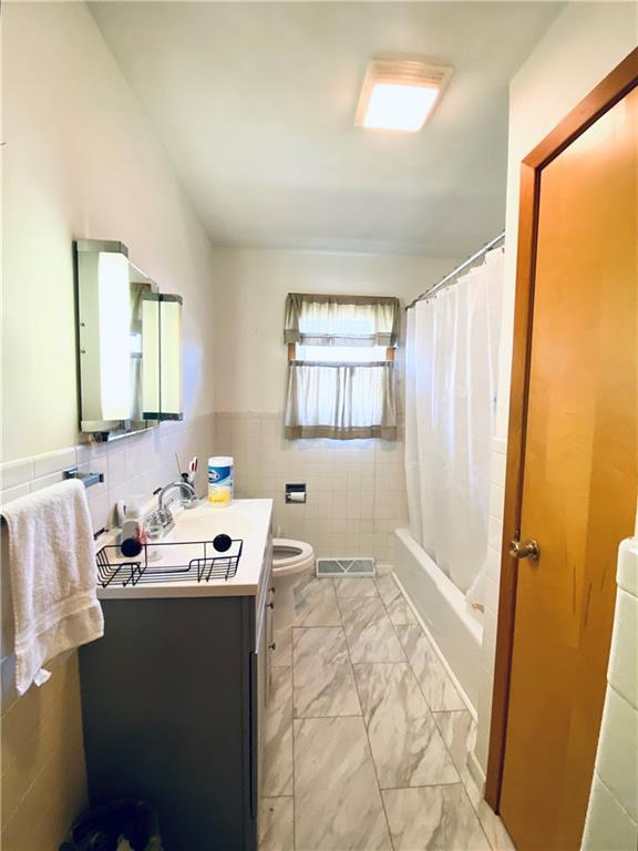 311 SW 12th Ter, Concordia, MO 64020 - full bathroom featuring tile walls, vanity, toilet, marble look tile flooring, and shower / bathtub combination with curtain
