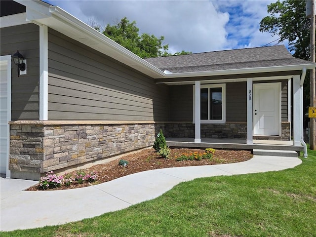 820 Carolina St, Neodesha, KS 66757 - view of exterior entry featuring covered porch, stone siding, a lawn, and roof with shingles