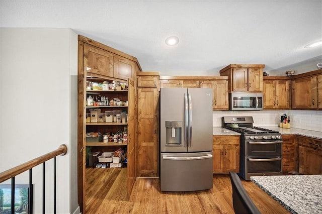 14115 NW 68th St, Parkville, MO 64152 - kitchen with stainless steel appliances, light wood finished floors, brown cabinetry, decorative backsplash, and light stone counters
