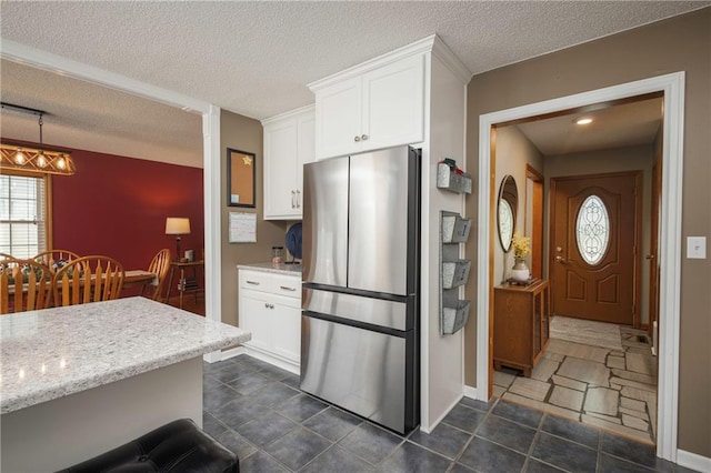 315 Goodrich Dr, Warrensburg, MO 64093 - kitchen with freestanding refrigerator, a textured ceiling, white cabinetry, and light stone counters