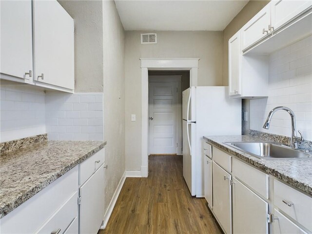 2416 E 22nd St, Kansas City, MO 64127 - kitchen featuring white cabinets, backsplash, dark wood finished floors, freestanding refrigerator, and light stone counters