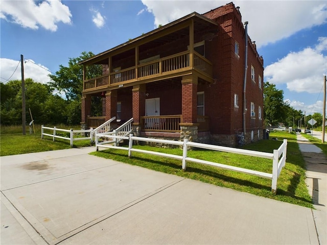 2416 E 22nd St, Kansas City, MO 64127 - view of front of house with a balcony, brick siding, a fenced front yard, and a porch