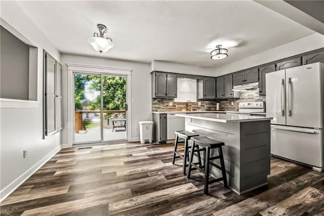 2004 NE Wien Ave, Blue Springs, MO 64029 - kitchen with white appliances, under cabinet range hood, dark wood-style flooring, tasteful backsplash, and light countertops