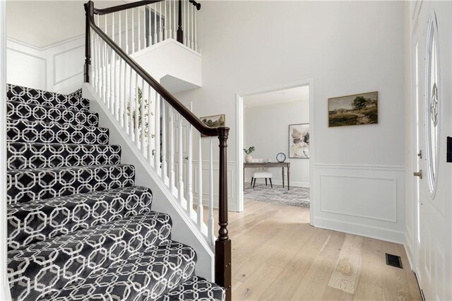 14600 Reinhardt Ln, Leawood, KS 66224 - staircase with hardwood / wood-style floors, a decorative wall, a towering ceiling, and a wainscoted wall