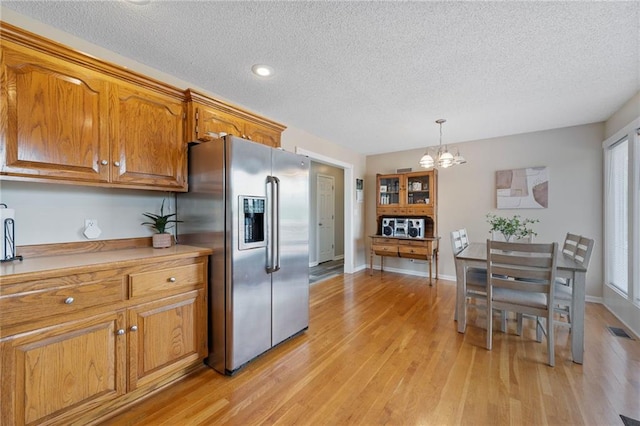 103 Bridgeport Dr, Smithville, MO 64089 - kitchen with stainless steel fridge, a chandelier, brown cabinetry, light wood-type flooring, and a textured ceiling