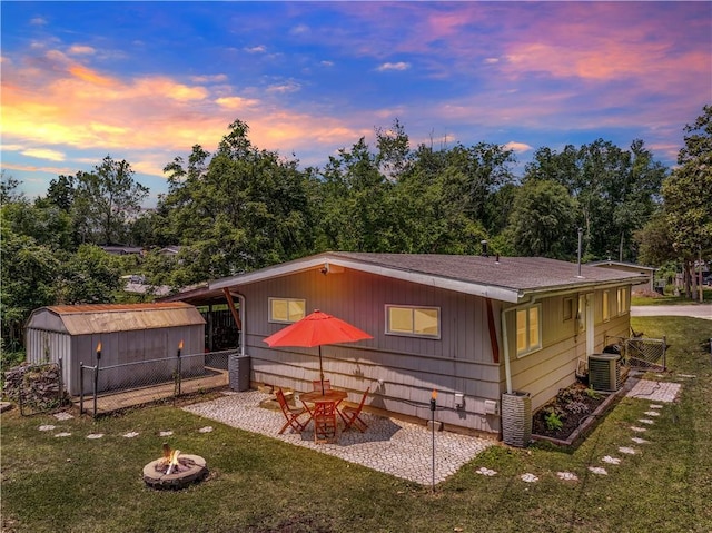 1112 Anderson St, Warrensburg, MO 64093 - back of property at dusk featuring a fire pit, a storage shed, a shingled roof, and a patio