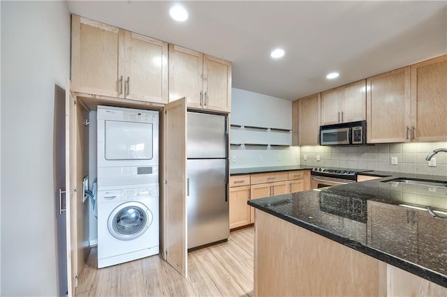 5008 Baltimore Ave Unit 102, Kansas City, MO 64112 - kitchen featuring stainless steel appliances, light brown cabinets, stacked washer / drying machine, dark stone counters, and recessed lighting