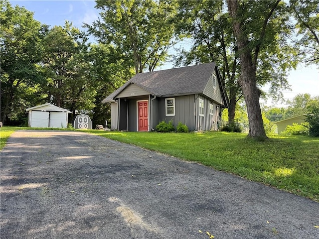 110 W 7th St, Knob Noster, MO 65336 - view of front of property featuring board and batten siding, a front lawn, roof with shingles, and a storage unit