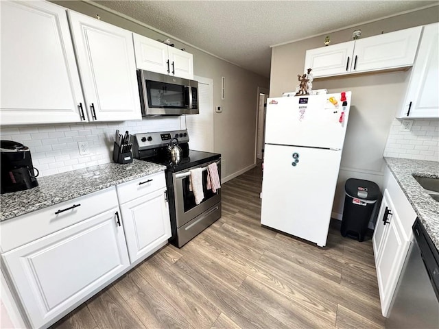 110 W 7th St, Knob Noster, MO 65336 - kitchen featuring appliances with stainless steel finishes, white cabinetry, light wood finished floors, backsplash, and light stone counters