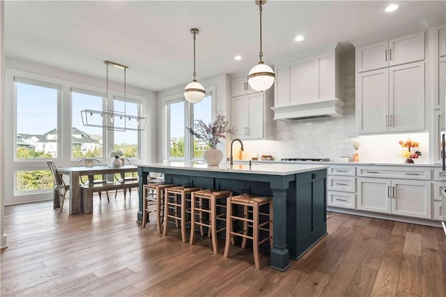 11594 S Zarda Dr, Olathe, KS 66061 - kitchen with premium range hood, wood finished floors, a breakfast bar area, light countertops, and white cabinetry