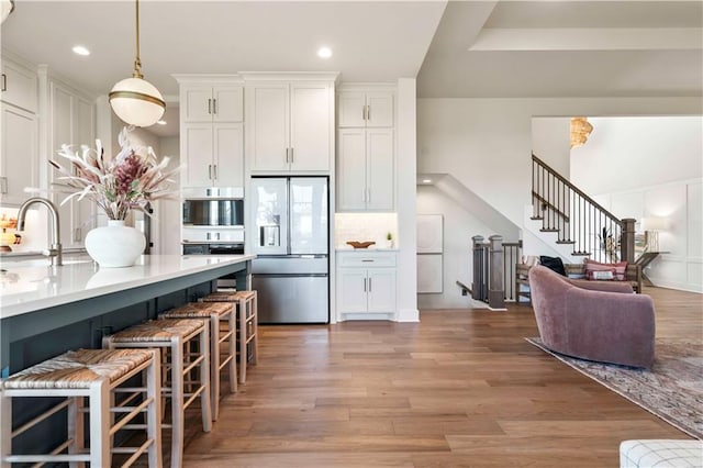 11594 S Zarda Dr, Olathe, KS 66061 - kitchen featuring stainless steel refrigerator with ice dispenser, white cabinets, a kitchen bar, light wood-style flooring, and recessed lighting